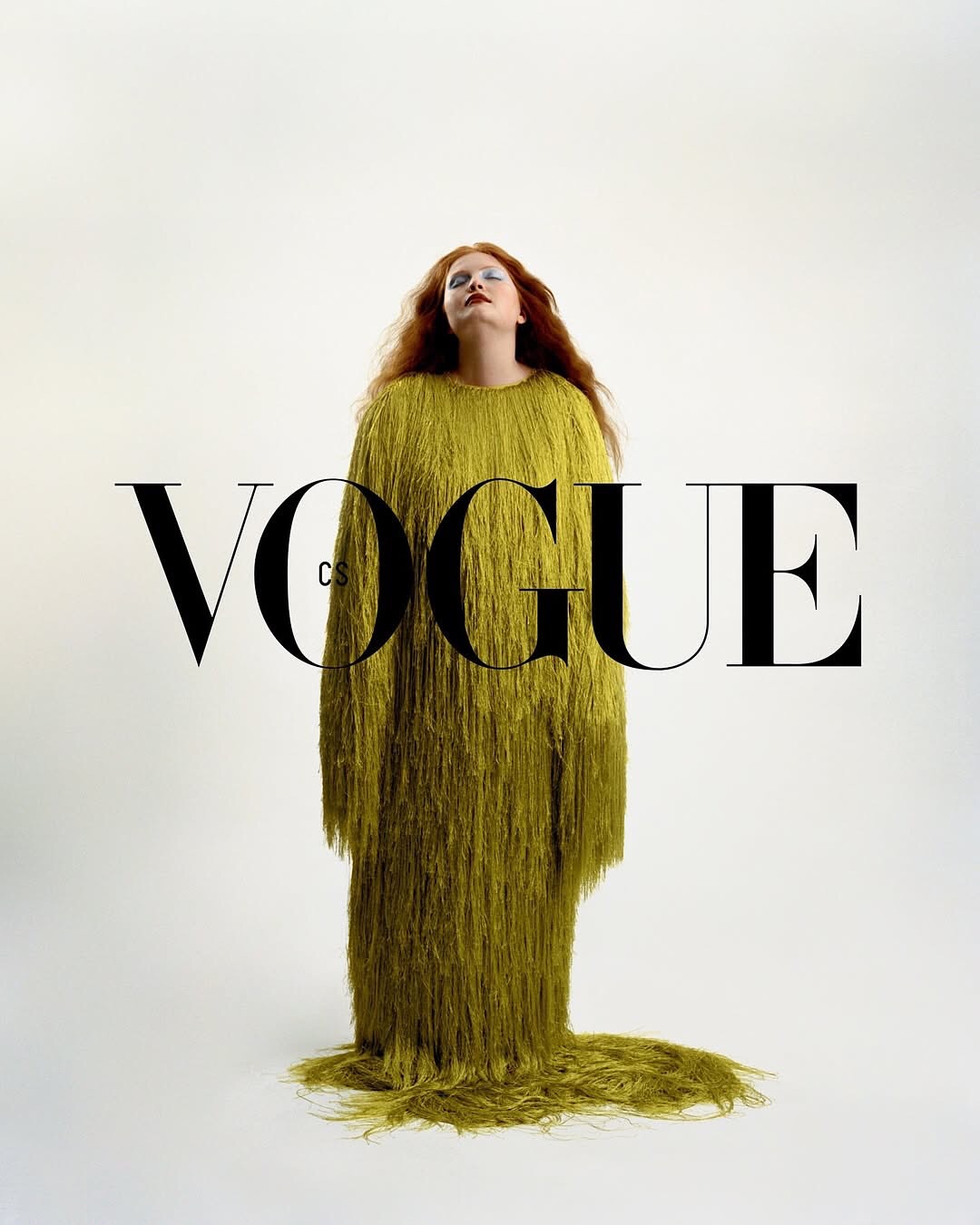 Vogue magazine cover featuring a red-haired woman in a full-length green fringed dress, standing against a white background.