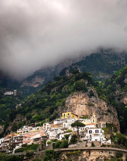 Picturesque view of Positano, Italy with its colorful buildings nestled into a hillside, partly shrouded in mist, on a cloudy day.