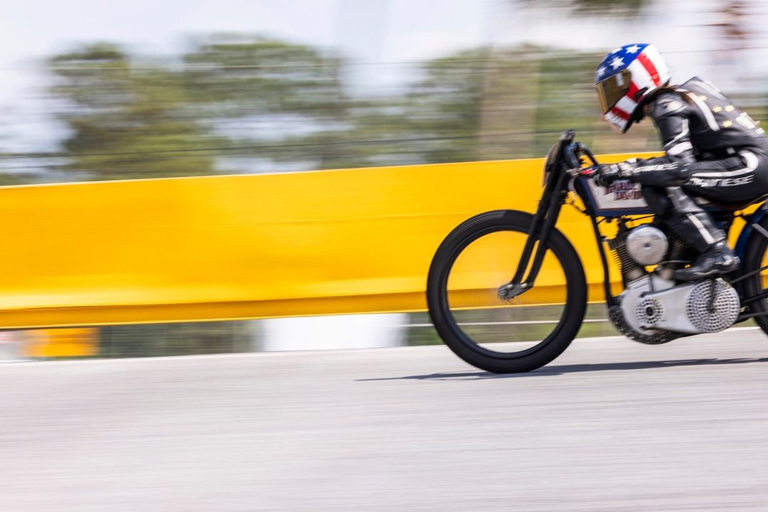 Motorcycle racer in American flag helmet speeds on track in leather gear. Extreme sports, outdoor environment, motion blur, yellow barrier.