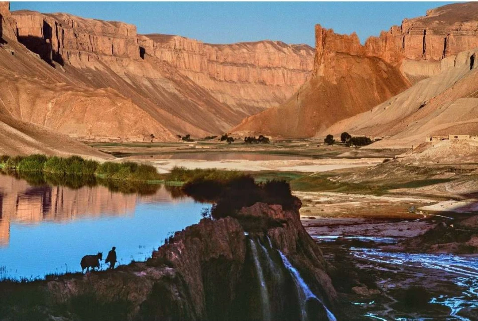 Scenic view of Band-e Amir lakes and mountains in Afghanistan with a person and animal silhouetted on a rocky outcrop.