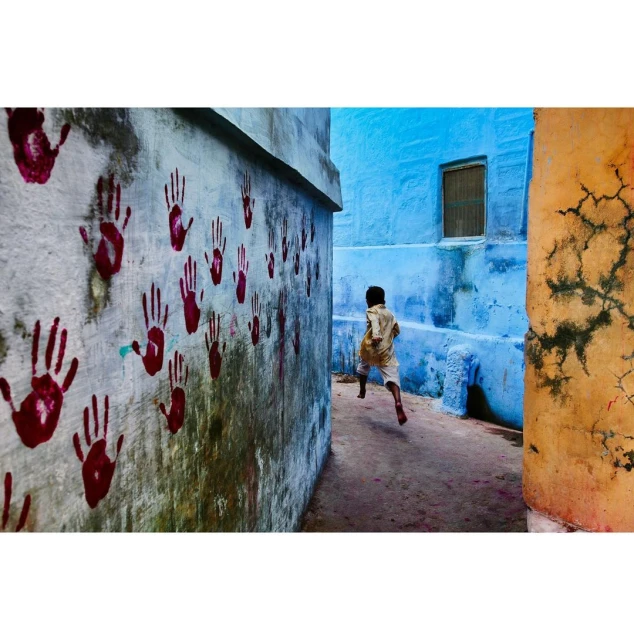 A child runs down a colorful alley with red handprints on a wall, showcasing vibrant travel and documentary photography.