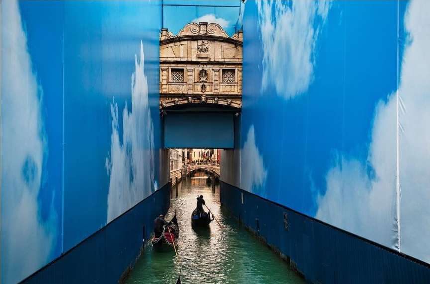 Two gondolas navigate a Venetian canal, framed by walls with cloud patterns and an architectural bridge backdrop, capturing the essence of Venice.