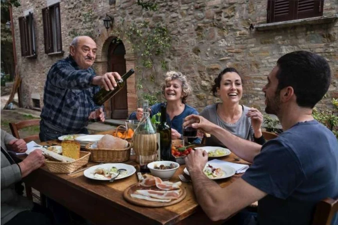 Group of people dining together outdoors at a rustic wooden table with wine and food, photographed by Steve McCurry.