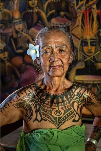 Elderly indigenous woman with traditional chest tattoo, wearing a white flower in her hair, artistic background and green cloth wrap.