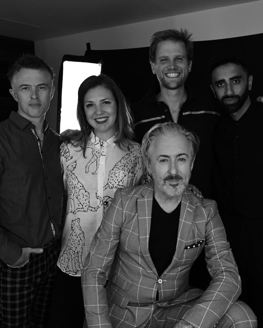 Group portrait in black and white featuring five individuals in a photo studio, two seated and three standing, posing for the camera.