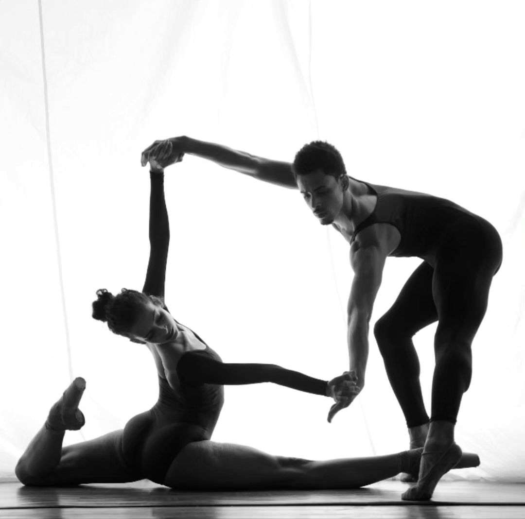 Monochrome photo of two ballet dancers, an adult man and adult woman, forming a square shape with their bodies against a white backdrop.