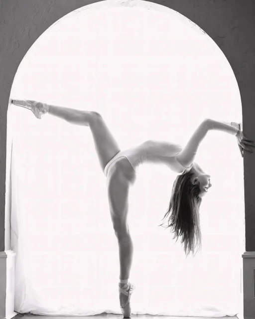 Black and white portrait of a ballerina in a white leotard, en pointe, bent over backwards, posing in an archway.