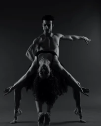 Two ballet dancers performing a dramatic lift against a dark studio background in black and white photography.