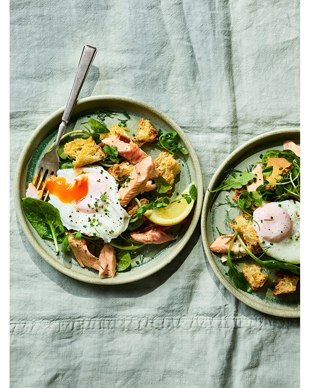 Overhead shot of two plates with salmon, poached eggs, croutons, and greens, creating a visually appetizing food composition.