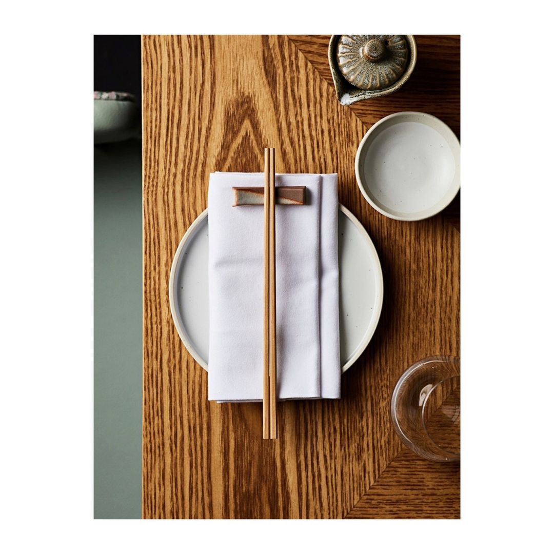 Overhead shot of a table setting with a plate, chopsticks, a white napkin, and a ceramic pot, creating an elegant and minimalist presentation.