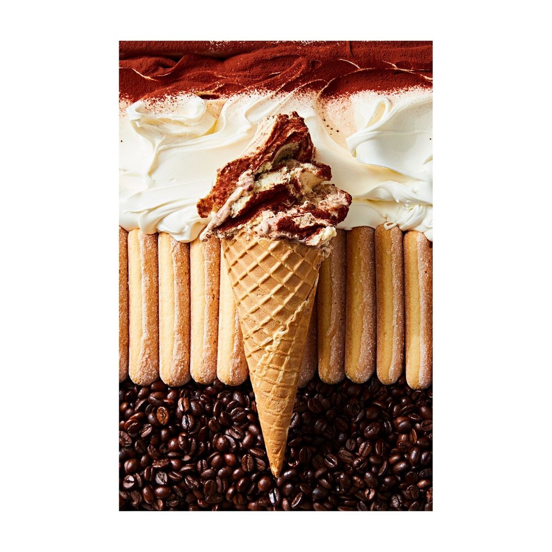 Overhead shot of tiramisu ice cream cone atop coffee beans and ladyfingers with cocoa powder and cream; food and beverage photography.