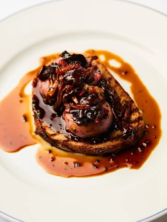 Close-up of a single slice of toast topped with meat and sauce, presented on a white plate with a blue rim, showcasing food photography.