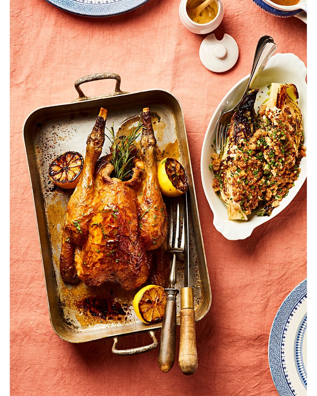 Overhead shot of roast chicken and grilled endives on a table with a light pink tablecloth and plates, highlighting a food photography.