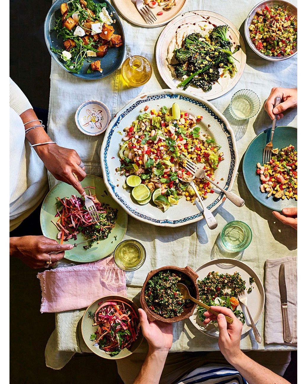 Overhead shot of a table set for a dinner party with multiple plates of colorful salads and vegetables being eaten by people.