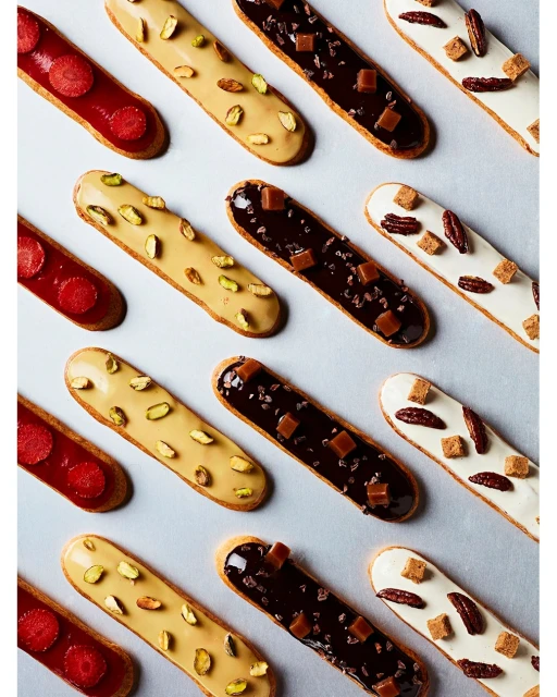 Overhead shot of an array of colourful eclairs. Flavours include strawberry, caramel, pistachio, chocolate and pecan in a clean food layout.
