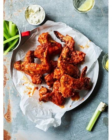 Overhead shot of flavorful buffalo chicken wings with celery sticks and dipping sauce on a grey surface, perfect for food photography.