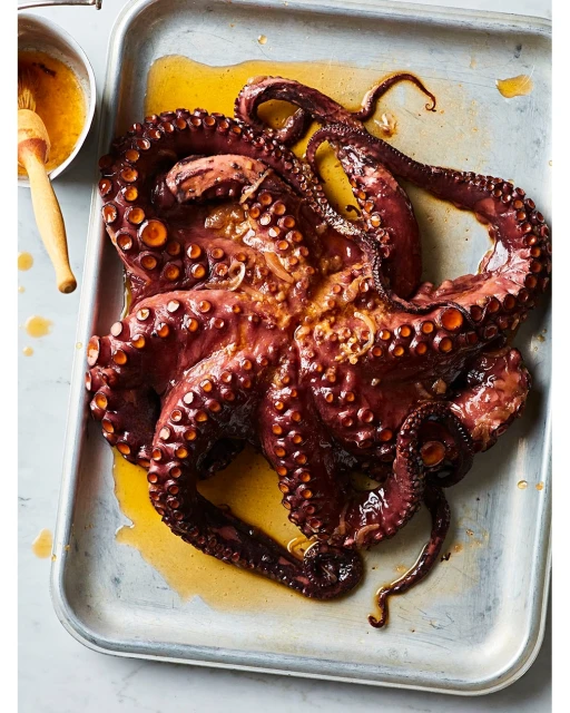 Overhead shot of a grilled octopus on a metal tray, drizzled with a yellow sauce, creating a visually appealing culinary presentation.