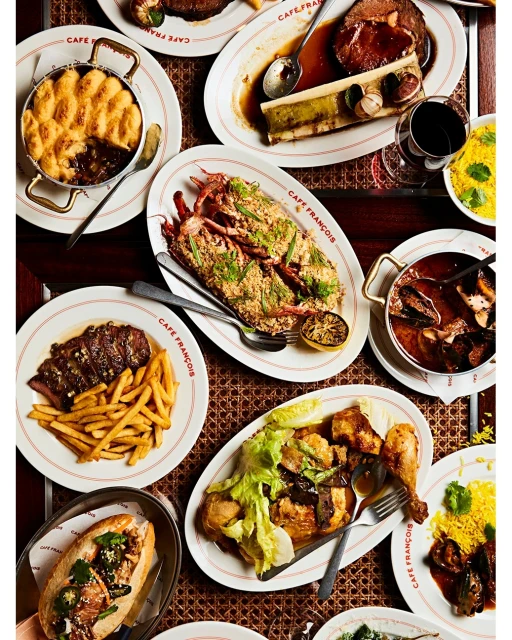Overhead shot of a variety of plated meals on a table, including lobster, bone marrow, french fries, and other dishes.
