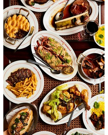 Overhead shot of a variety of plated meals on a table, including lobster, bone marrow, french fries, and other dishes.