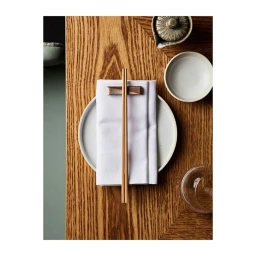 Overhead food photography of a white plate with folded white napkin and wooden chopsticks on a textured oak table.