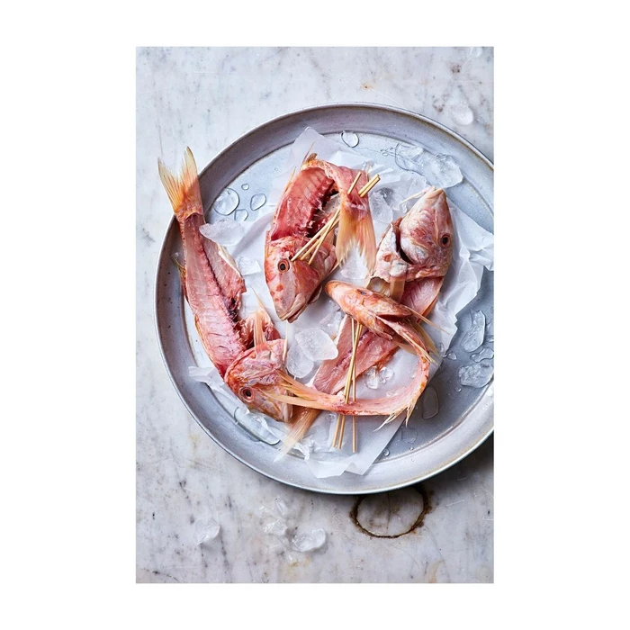 Dressed red mullet fish with skewers on white parchment paper inside a round metal tray on marble