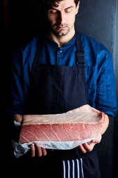 Chef in blue shirt and black apron holding a large raw fish loin in London, photographed by Steven Joyce.