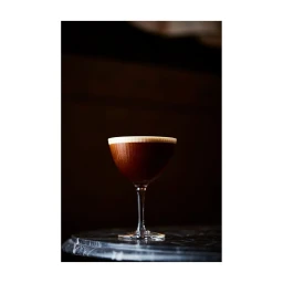 An espresso martini in a coupe glass resting on a dark marble table against a moody, softly lit background.