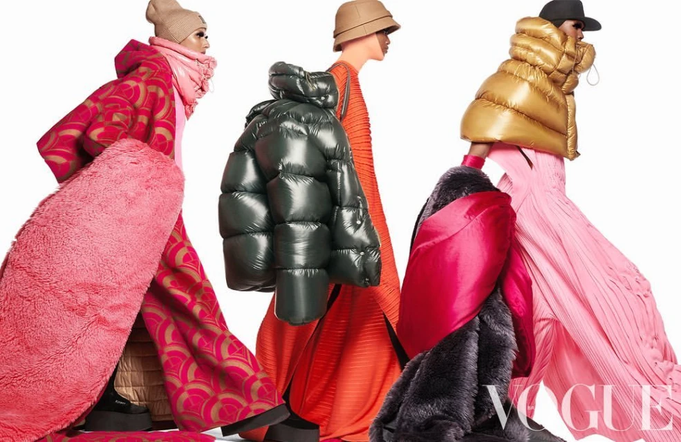 Fashion editorial shot showcasing three models in vibrant outerwear and pleated dresses against a clean white backdrop with 'Vogue' branding.