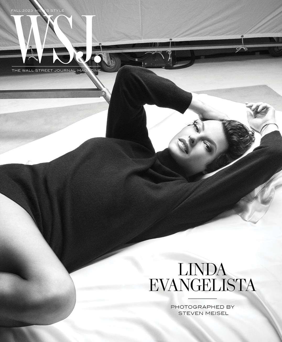 Linda Evangelista lies on white fabric wearing a dark sweater, featured on the cover of WSJ Magazine Fall 2023