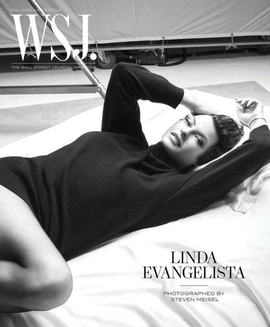 Linda Evangelista lies on white fabric wearing a dark sweater, featured on the cover of WSJ Magazine Fall 2023
