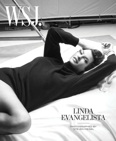 Linda Evangelista lies on white fabric wearing a dark sweater, featured on the cover of WSJ Magazine Fall 2023