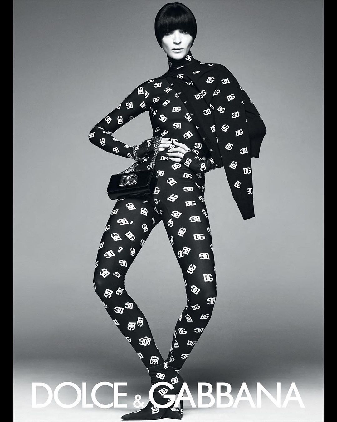 Model in black and white patterned catsuit wearing matching heels and holding a handbag by Steven Meisel