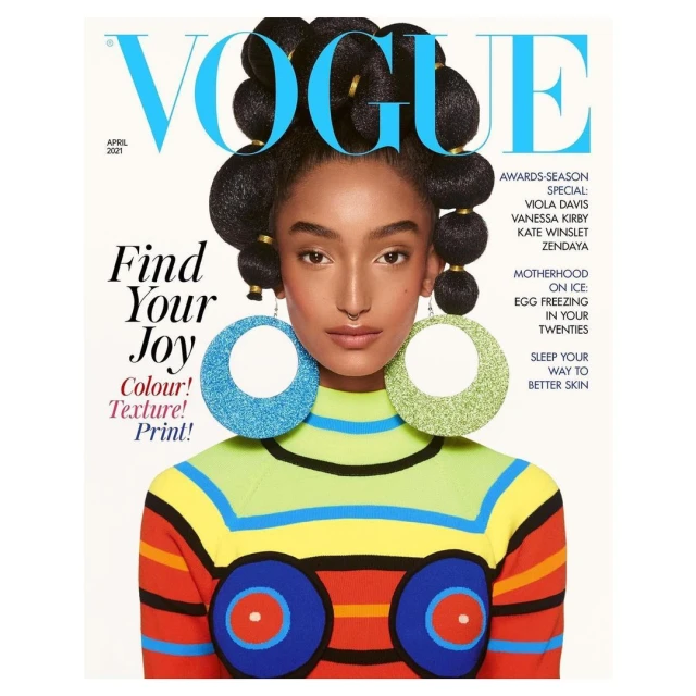 Vogue cover featuring a Black model with large hoop earrings and a colorful striped sweater. Magazine cover, close-up studio shot.