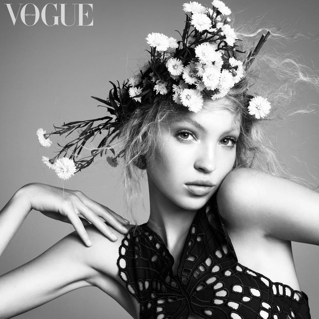 Black and white portrait of a woman wearing a large floral crown made of white daisies and a cut-out black top.