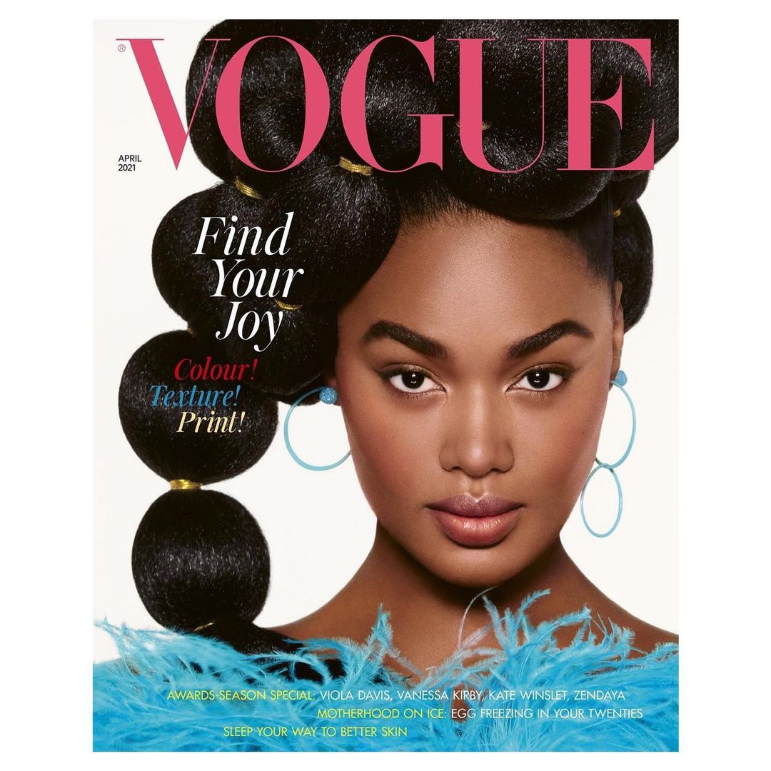 Vogue cover featuring a Black female model with a voluminous updo, hoop earrings, and a turquoise feather boa against a white background.