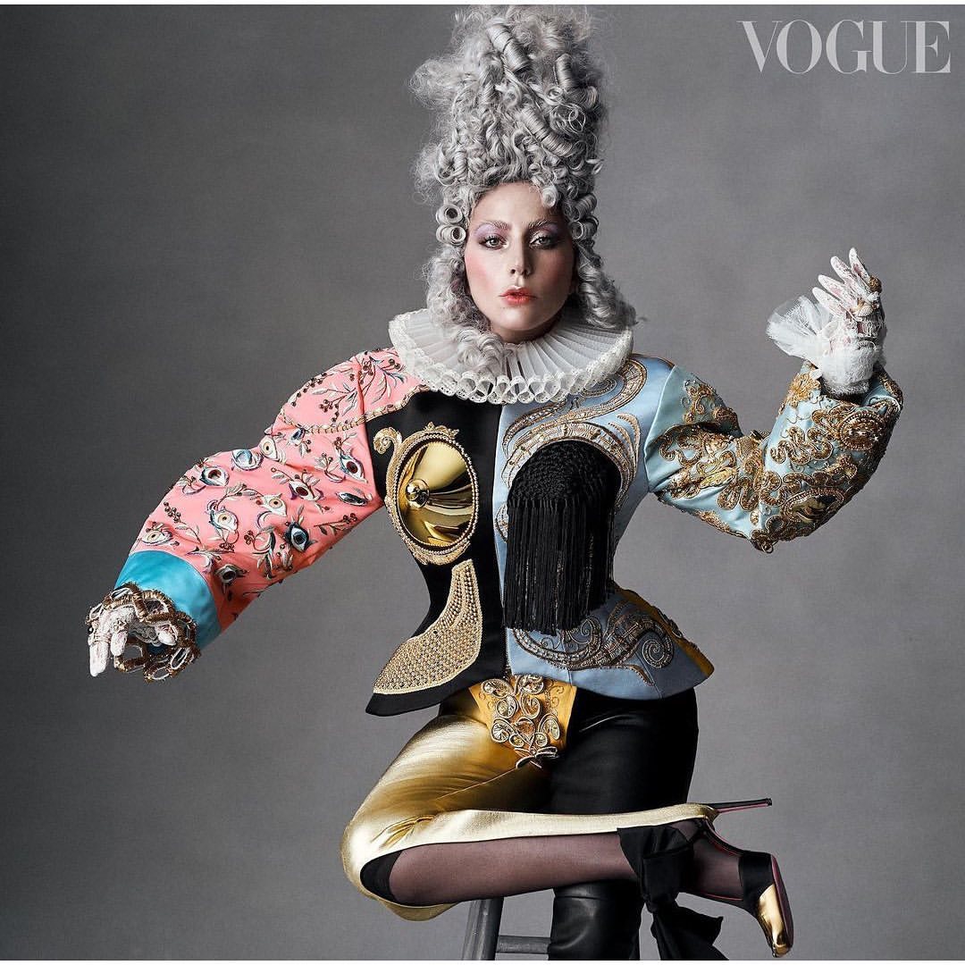 Lady Gaga in dramatic theatrical costume and ornate wig, seated in photo studio for Vogue magazine cover, captured in high fashion photography.