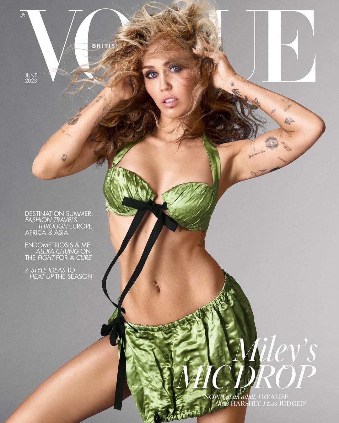 Miley Cyrus on the cover of British Vogue, June 2023. She poses in a green satin lingerie set with dark bows against a grey backdrop.