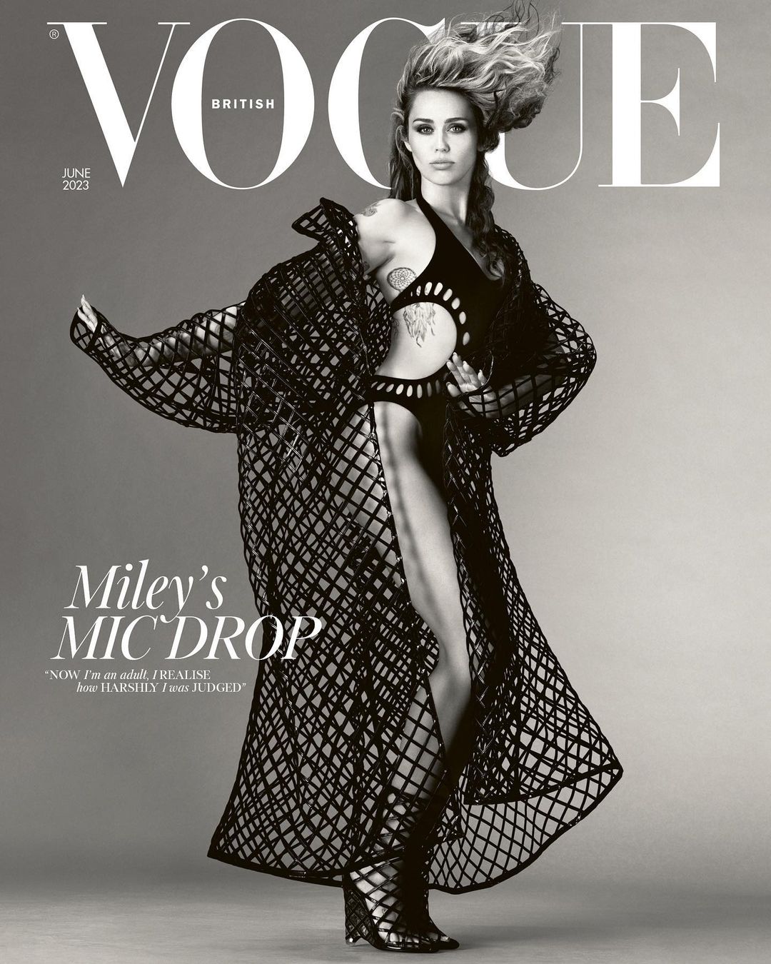 Miley Cyrus on the cover of British Vogue June 2023, wearing a black cut-out bodysuit and matching net-like long coat and gladiator heels.