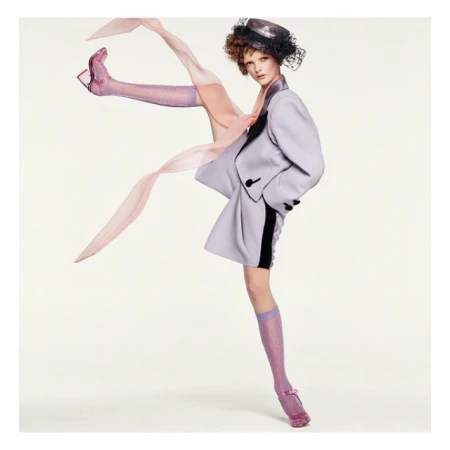 Fashion editorial shot: A woman in a pale purple suit and sparkly socks poses against a bright white backdrop with light pink accents.