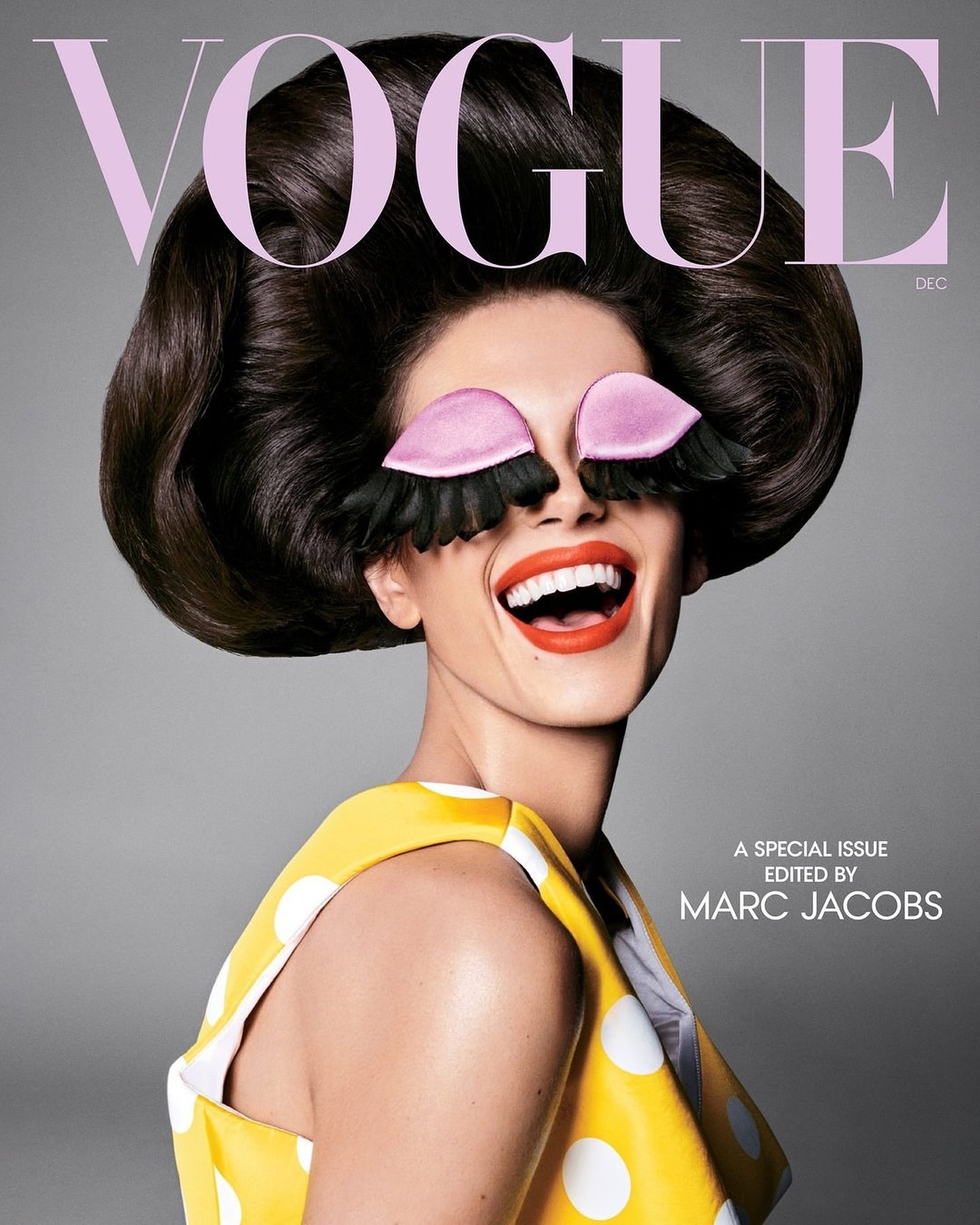 Vogue cover featuring a woman with high-volume dark hair, wearing yellow polka dot dress and oversized novelty eyelashes, smiling widely.