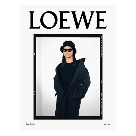Fashion advertisement featuring a man in sunglasses, a bucket hat, and a long coat against a white background, framed by a black border with text.