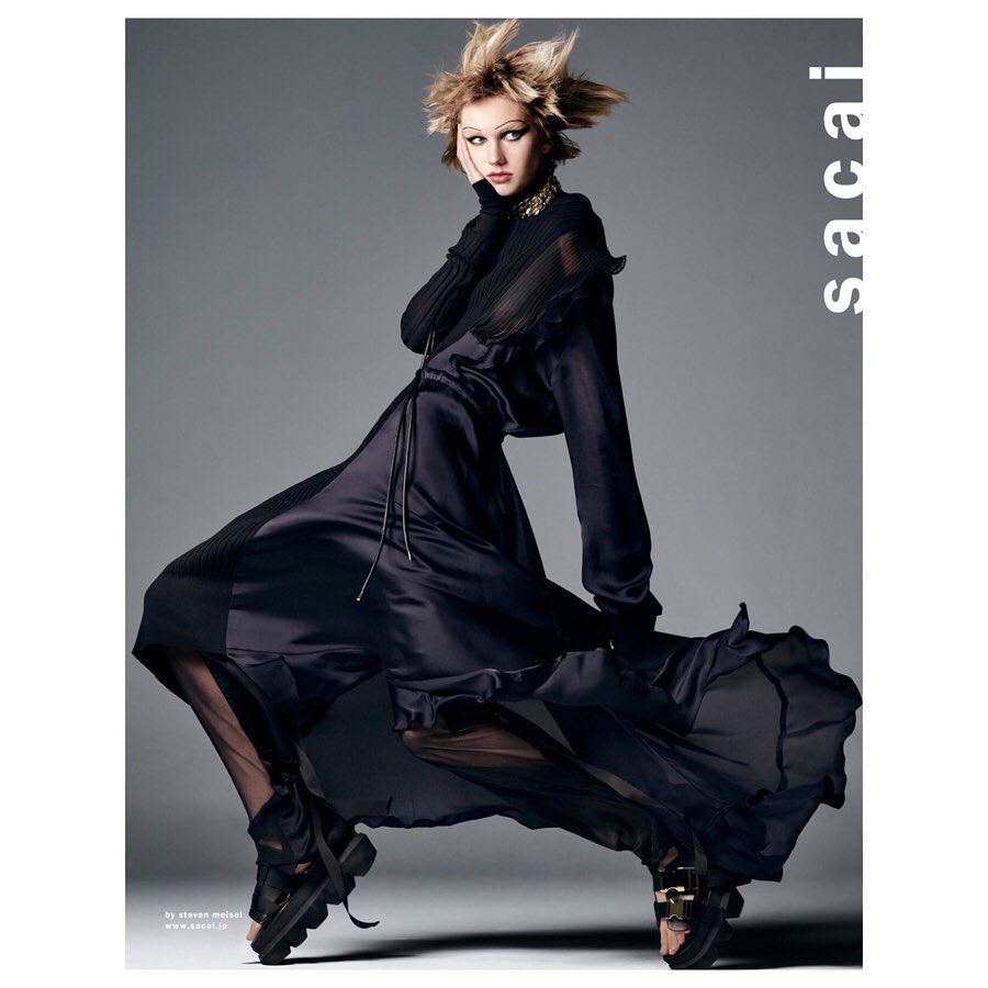 A high-fashion shot shows a model in a dark dress with a spiky hairdo, posed in a studio against a gray background, wearing chunky platform shoes.