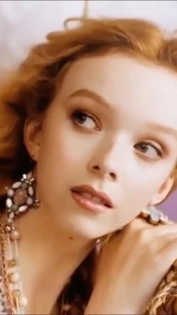 Close-up portrait of a woman with red hair wearing ornate statement earrings and a necklace, looking upward.