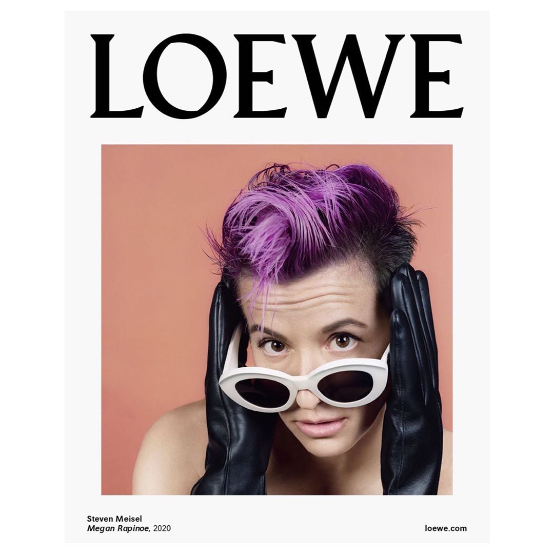 Fashion magazine cover featuring a woman with purple hair wearing sunglasses and black gloves against an orange background.