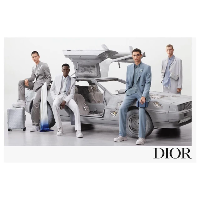 Four adult male models pose with a weathered DeLorean automobile against a plain background, highlighting fashion and automotive elements.