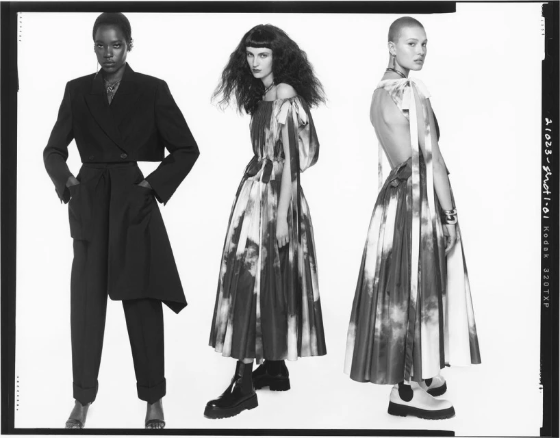 Black and white fashion studio shot showcases three female models in high-fashion garments, including a cropped suit jacket and abstract dresses.