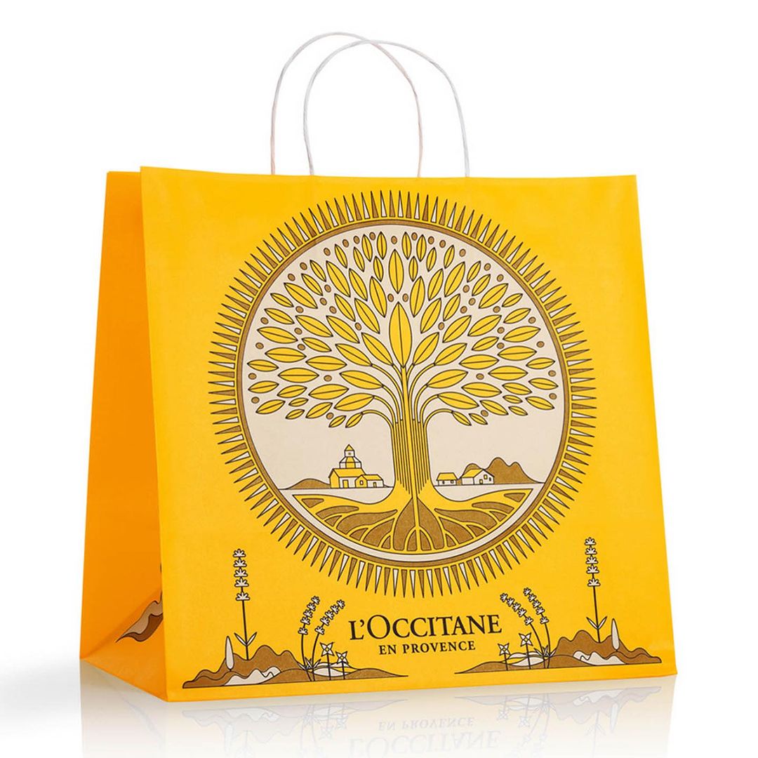 Yellow shopping bag from L'Occitane featuring an illustrative tree design, set against a clean white background with soft studio lighting.