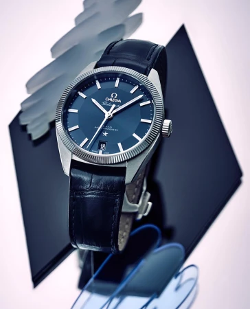 Close-up studio shot of a stainless steel Omega Constellation watch with a blue dial and black leather band on abstract display.