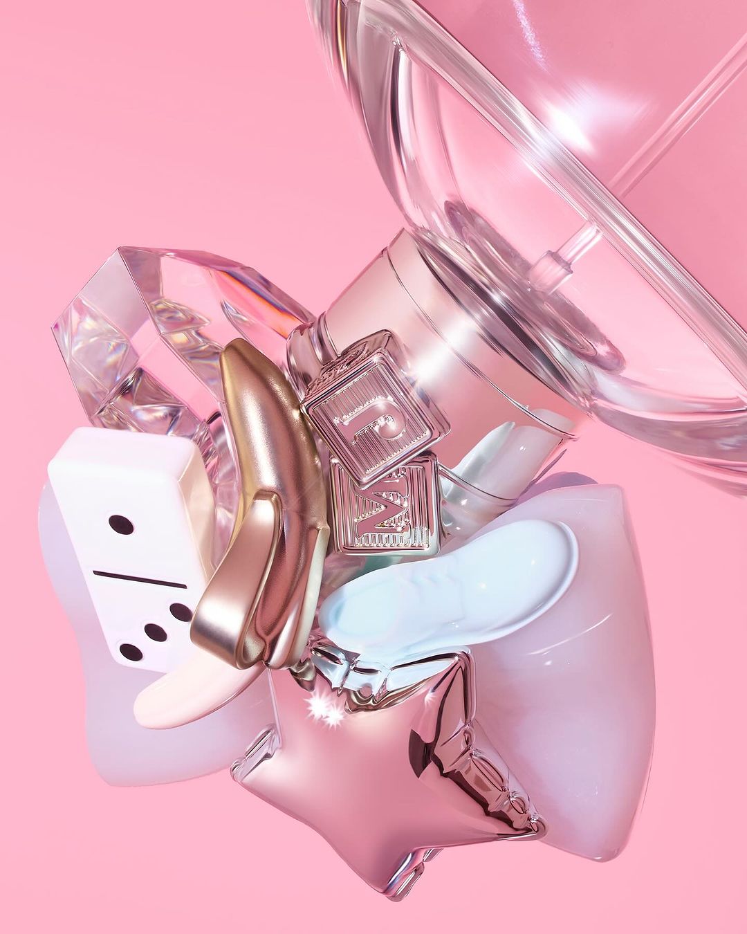 Still life of objects including a shoe, dice, perfume bottles, and star balloon against a light pink backdrop in a studio.