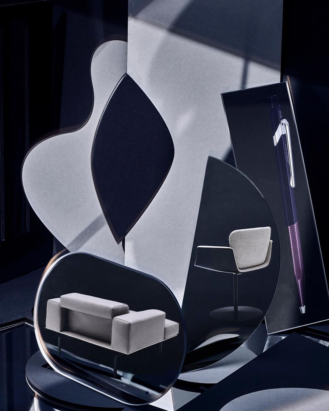 Furniture product shoot featuring a modern grey couch and chair against a dark background with abstract geometric shapes and artistic composition.
